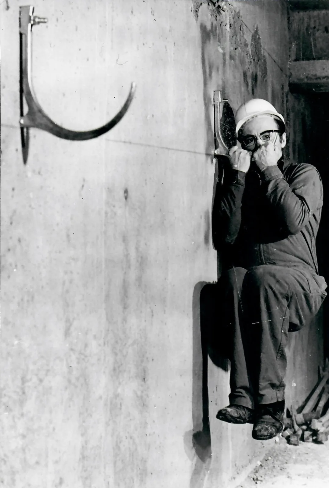 Photo d'archive Celt, un ouvrier assis sur un support de canalisation fixé au mur béton